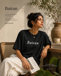 Woman wearing a black 'Bairan' t-shirt sitting on a chair with a plant and vase in the background.