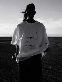 Person wearing a white t-shirt with 'empty is enough' text in a black and white landscape.